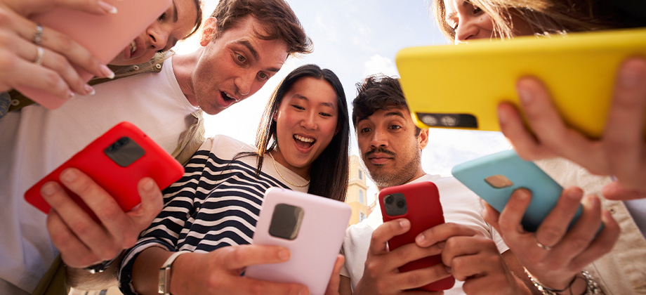 diverse young people circle looking surprise at phone together outdoors