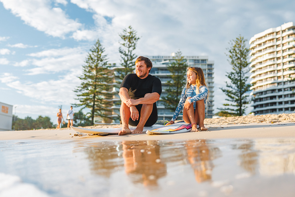father and daughter sitting on surfboards gold coast beach
