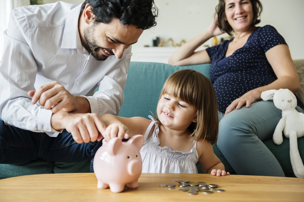 Father helping daughter put money into piggy bank