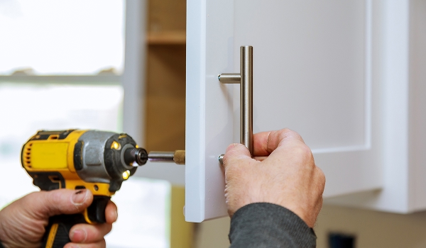 person using a power drill to secure a handle to a white cabinet door