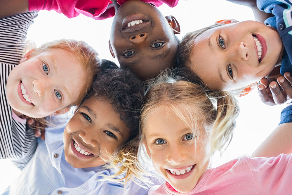 Five multi ethnic children with their heads together looking at camera from above