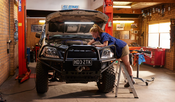 Person performing maintenance on a four-wheel-drive vehicle in a workshop with the bonnet open.