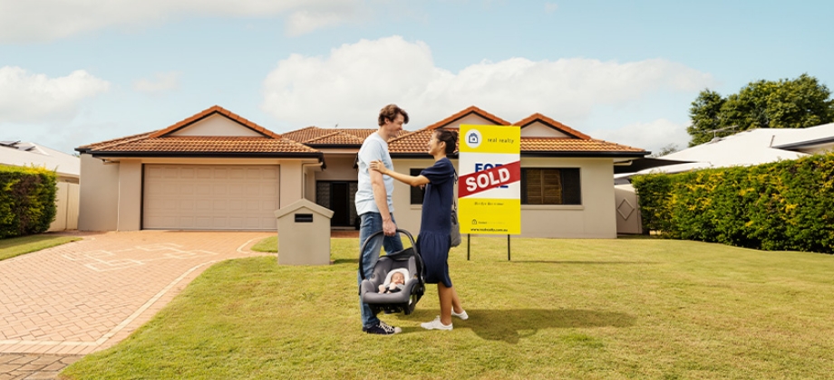 Young family standing in front of home with sold sign